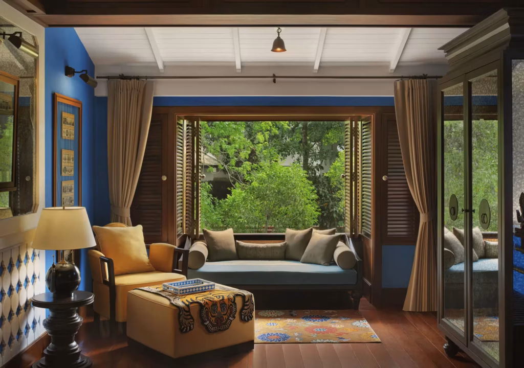 Riverside Suite living area at Rosewood Luang Prabang with cobalt walls, teak daybed, and a garden view.