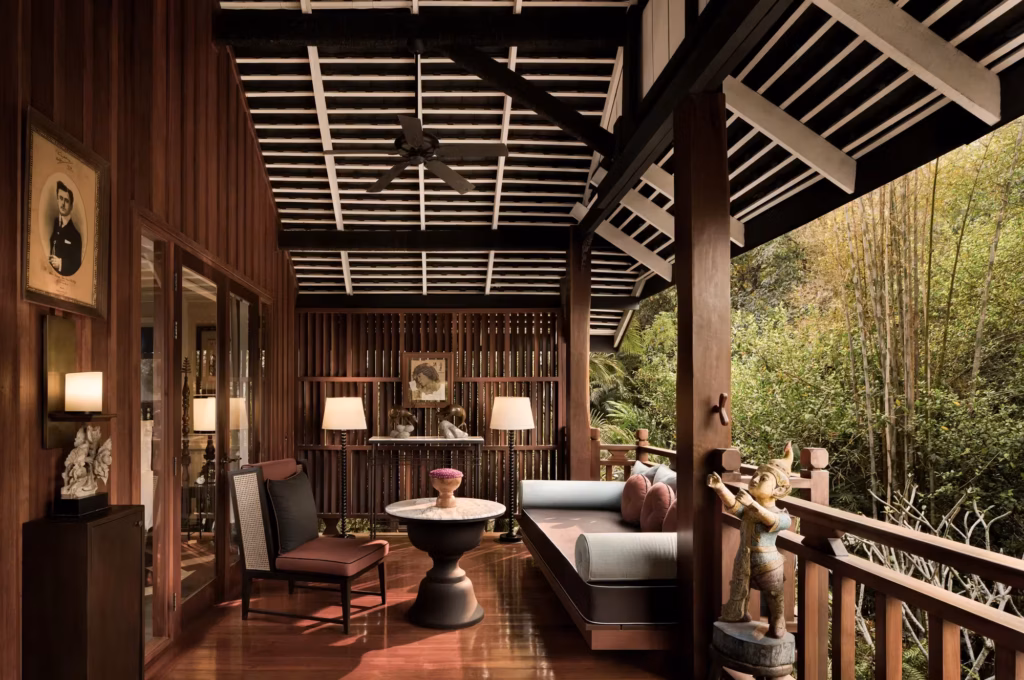 Riverside Villa terrace at Rosewood Luang Prabang with teak beams, a sage daybed, and views into bamboo forest.