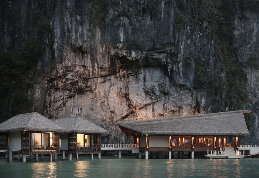 Overwater villas and an open-air pavilion at Lagen Island Resort in El Nido, Palawan, set against a dramatic limestone cliff.