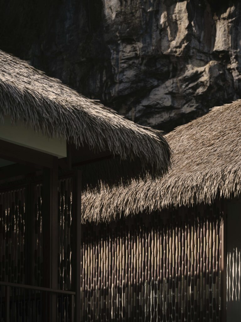 Close-up of thatched roofs and woven bamboo screens at Lagen Island Resort in El Nido, Palawan, framed by limestone cliffs.