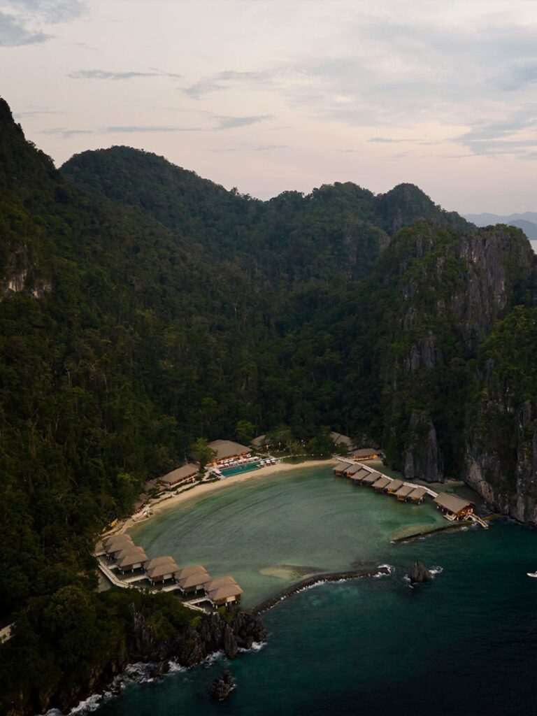 Aerial view of Lagen Island Resort in El Nido, Palawan, with overwater villas surrounding a turquoise cove beneath limestone cliffs.