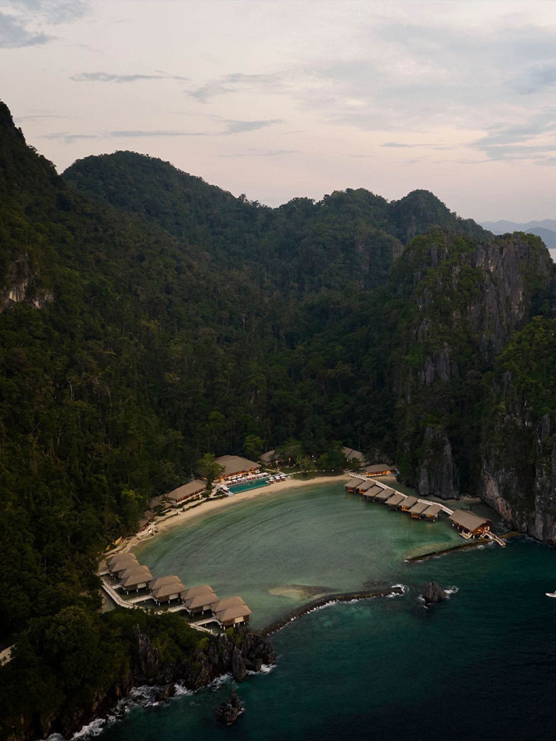 Aerial view of Lagen Island Resort in El Nido, Palawan, with overwater villas surrounding a turquoise cove beneath limestone cliffs.