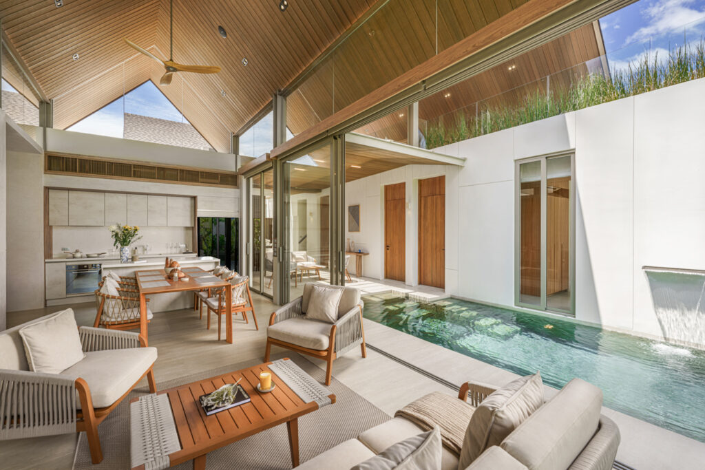 ANSAYA Phuket villa interior in Phuket, Thailand, with open-plan living and dining areas, a pitched timber ceiling, floor-to-ceiling glass doors, and private courtyard swimming pool.