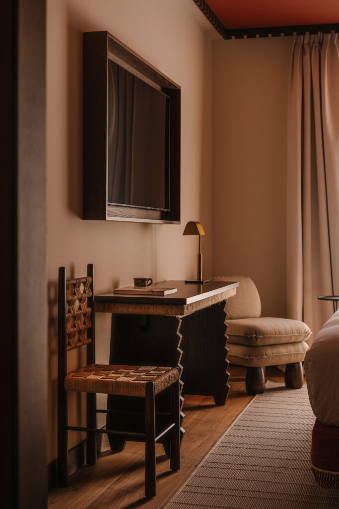 Desk corner in a King Cuzco room at Palacio de Godoy, Cáceres, Curio Collection by Hilton, with a woven rush-seat chair, a dark wood writing desk, a brass task lamp, a framed wall mirror, and a linen slipper chair.