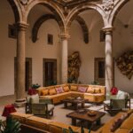 Courtyard of Palacio de Godoy Cáceres, Curio Collection by Hilton, where interior designer Szymon Keller pairs the 16th-century Renaissance stone arcade with ochre sofas, sage-green armchairs, and Peruvian-patterned cushions.