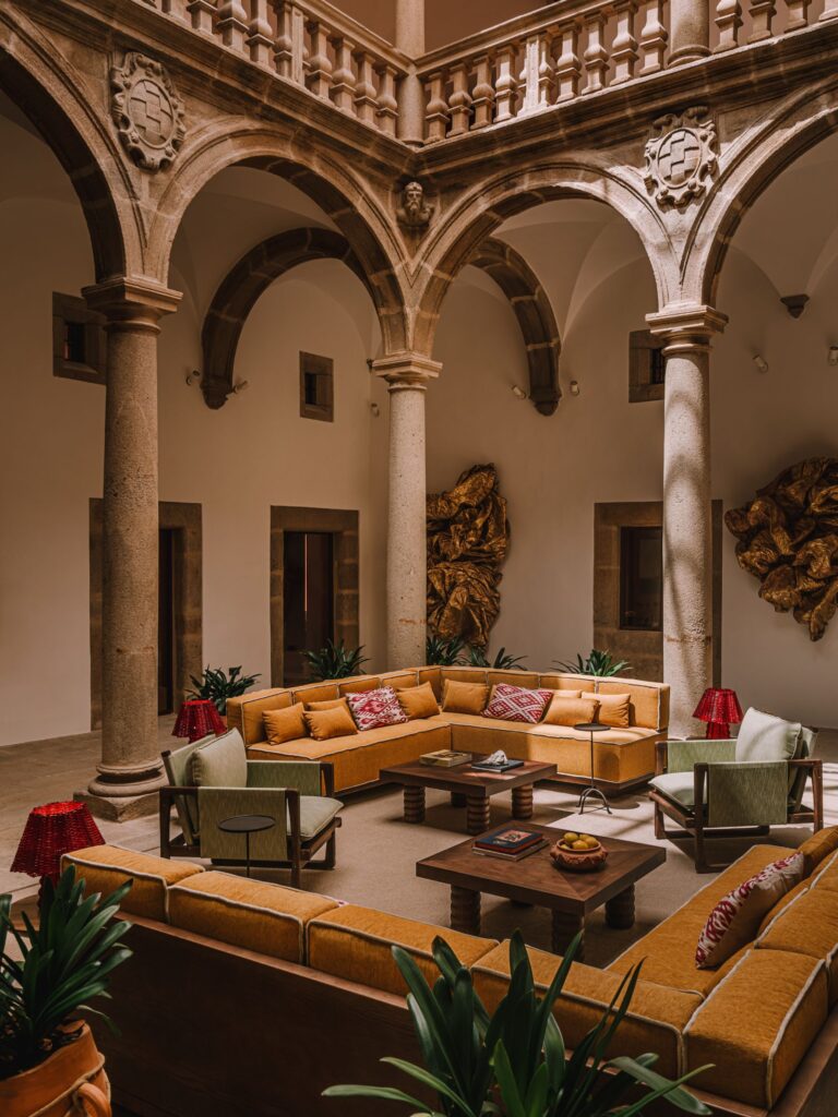 Courtyard of Palacio de Godoy Cáceres, Curio Collection by Hilton, where interior designer Szymon Keller pairs the 16th-century Renaissance stone arcade with ochre sofas, sage-green armchairs, and Peruvian-patterned cushions.