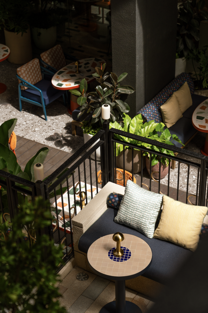 Terraced outdoor seating with terrazzo tables, black railings and tropical planting, seen from above.