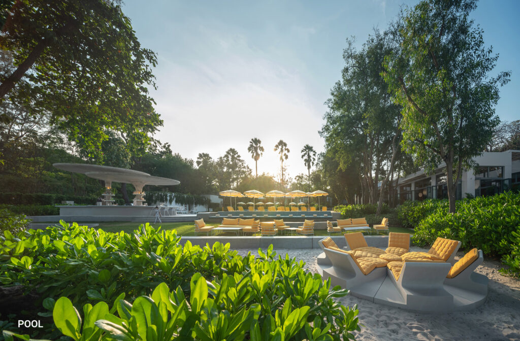 Poolside landscape at The Standard, Hua Hin, Thailand, with yellow lounge seating, striped umbrellas, mature trees, and tropical gardens designed by Shma.