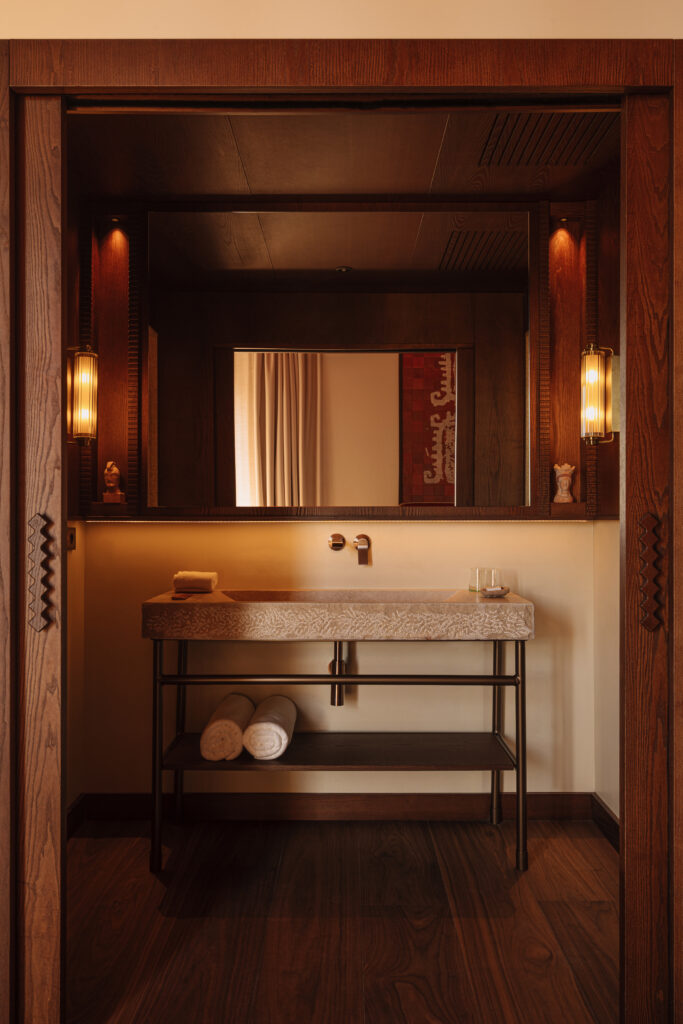 Suite bathroom at Palacio de Godoy, Cáceres, with a carved stone basin on a black metal stand and fluted glass sconces.