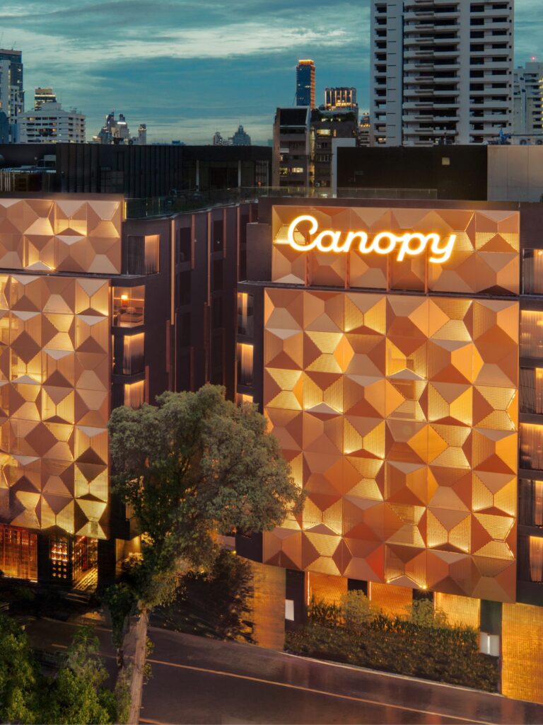 Canopy by Hilton Bangkok Sukhumvit exterior at dusk, featuring an illuminated geometric façade against the Bangkok skyline.