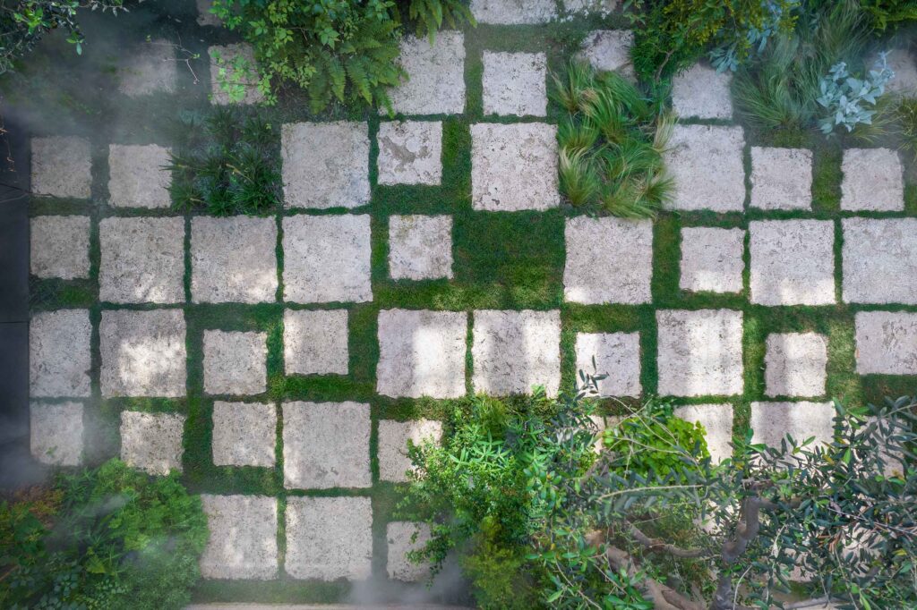 Local travertine stone pavers with greenery growing between them, forming a garden path at Botanica Meditation Center.