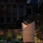 Illuminated travertine structure with angular walls amid garden planting and stone paths at Botanica Meditation Centre by HAS design and research in Hefei, China.