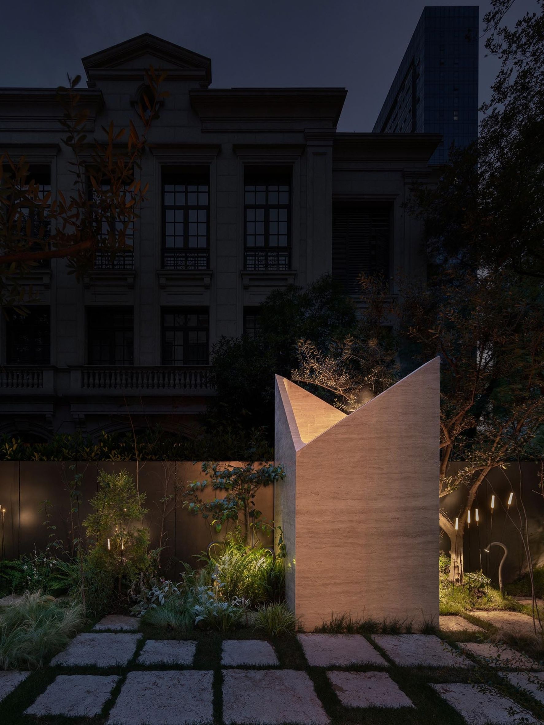 Illuminated travertine structure with angular walls amid garden planting and stone paths at Botanica Meditation Centre by HAS design and research in Hefei, China.