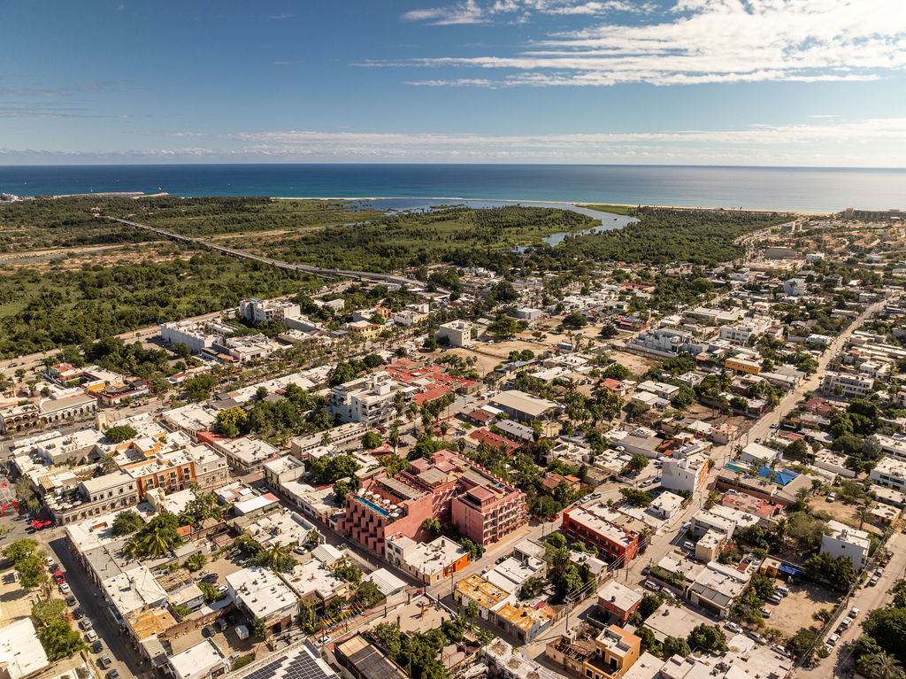Aerial view of San José del Cabo's historic center, with Laiva Plaza hotel by RA! visible in pink against the surrounding urban fabric. The Sea of Cortez sits a short distance beyond.