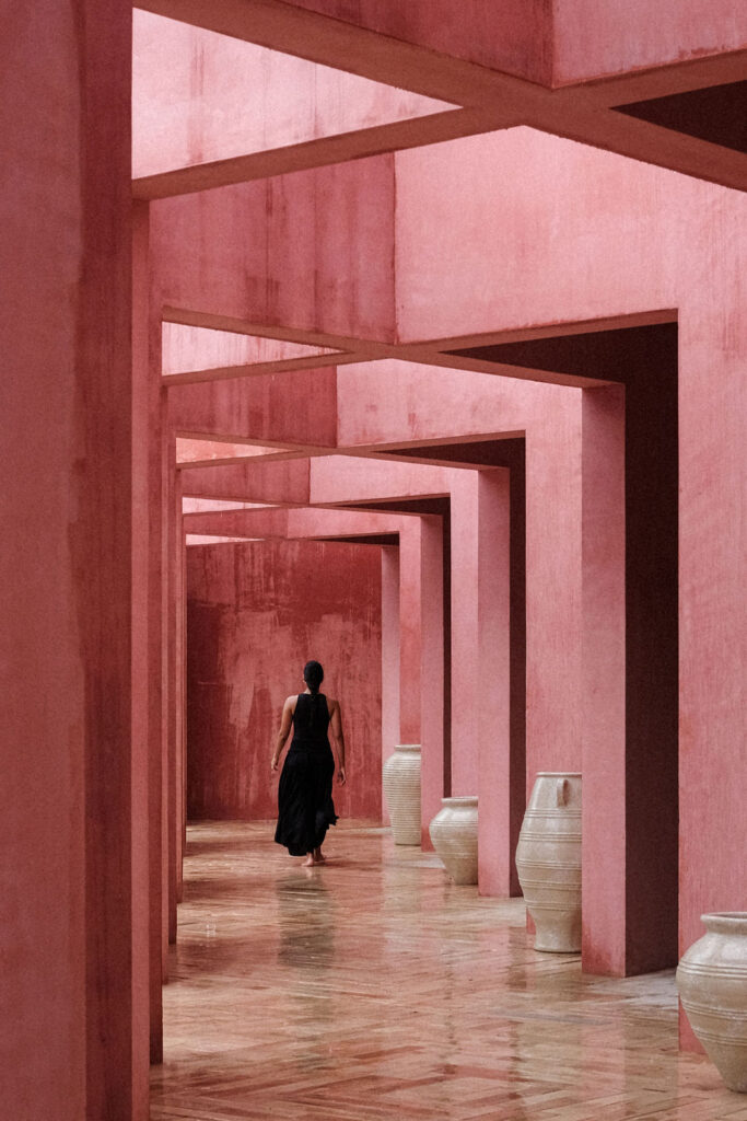 The interior corridor of Laiva Plaza hotel by RA! Repeated Rosa Mexicano handcrafted stucco frames recede in sequence alongside handmade ceramic vessels, translating the rhythm of papel picado into the interior.