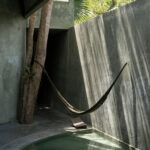 Casa Gruta in Yucatán, Mexico, designed by Salvador Román Hernández and Adela Mortera Villarreal, featuring a hammock suspended above a private pool in a concrete courtyard surrounded by tropical trees.