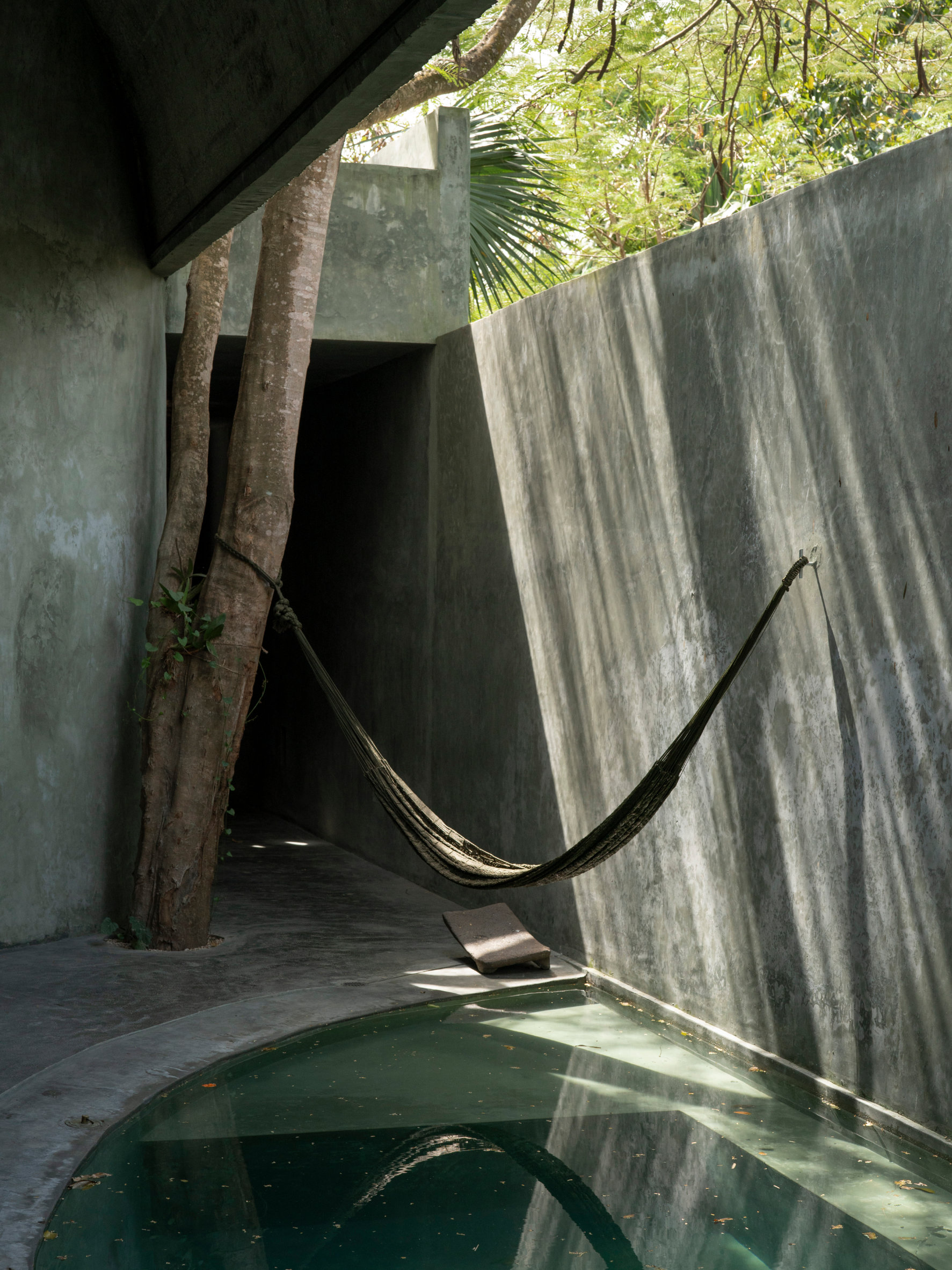 Casa Gruta in Yucatán, Mexico, designed by Salvador Román Hernández and Adela Mortera Villarreal, featuring a hammock suspended above a private pool in a concrete courtyard surrounded by tropical trees.