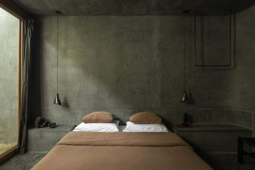 Bedroom at Casa Gruta in Yucatán, Mexico, featuring textured concrete walls and a bed with earthy brown linens.