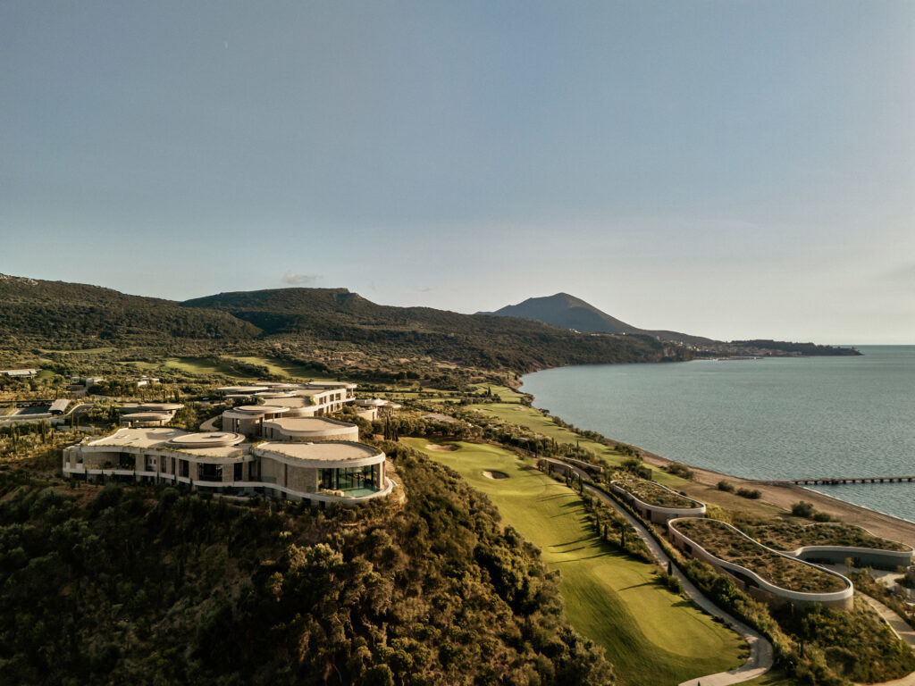 Aerial view of Mandarin Oriental, Costa Navarino above the bay of Navarino, Greece, with stone buildings and green-roofed villas.
