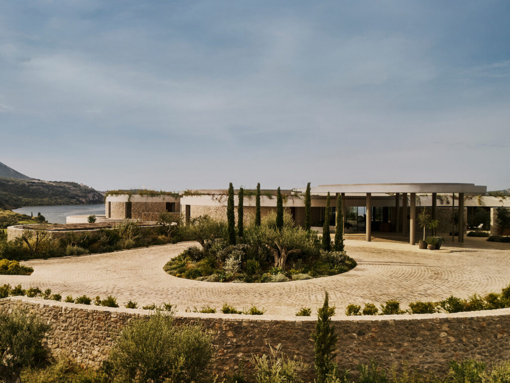 Entrance canopies at Mandarin Oriental, Costa Navarino, Greece, framed by cypress and olive trees along a cobblestone drive.