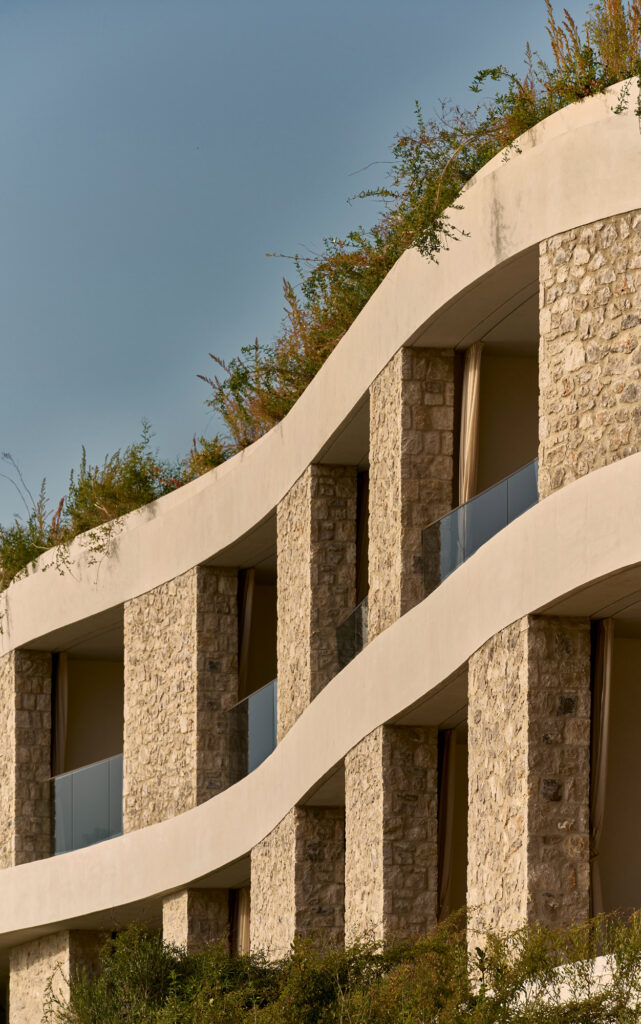 Curving stone and plaster facade of guest rooms at Mandarin Oriental, Costa Navarino, Greece, with a planted roof above.