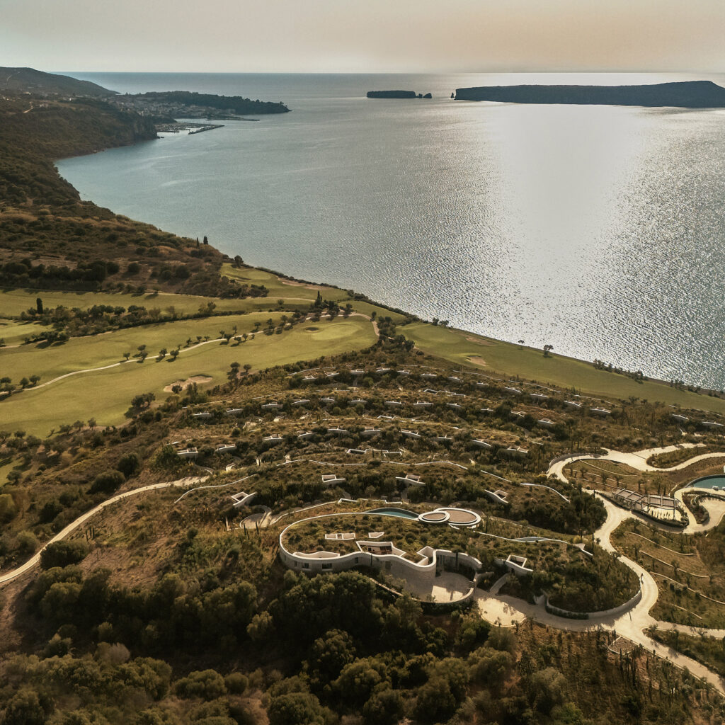 Aerial view of Mandarin Oriental, Costa Navarino above the bay of Navarino, Greece, with stone buildings and green-roofed villas.